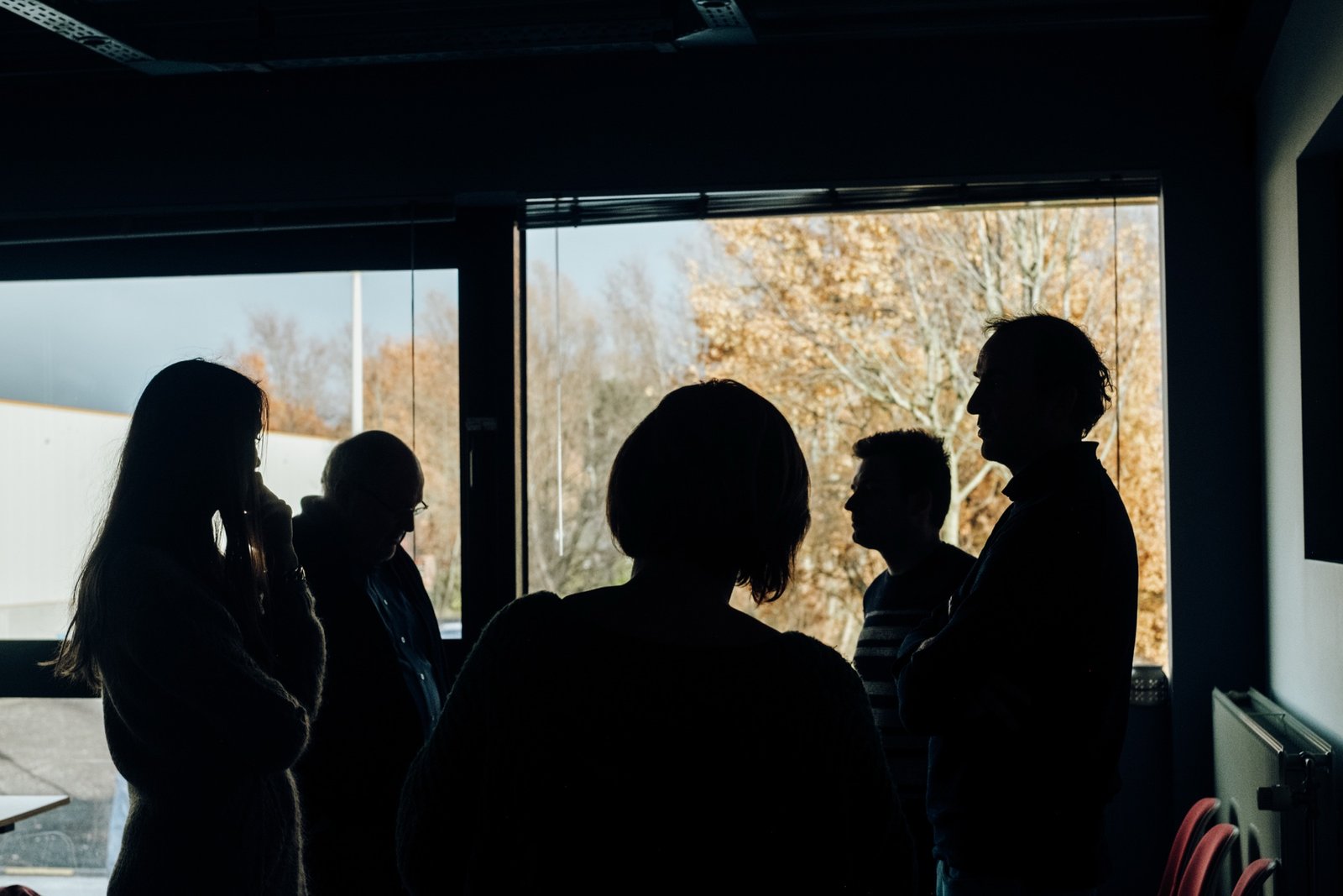 Silhouetten van een groep mensen die luistert en samen in gesprek is, tegenlicht van een raam
