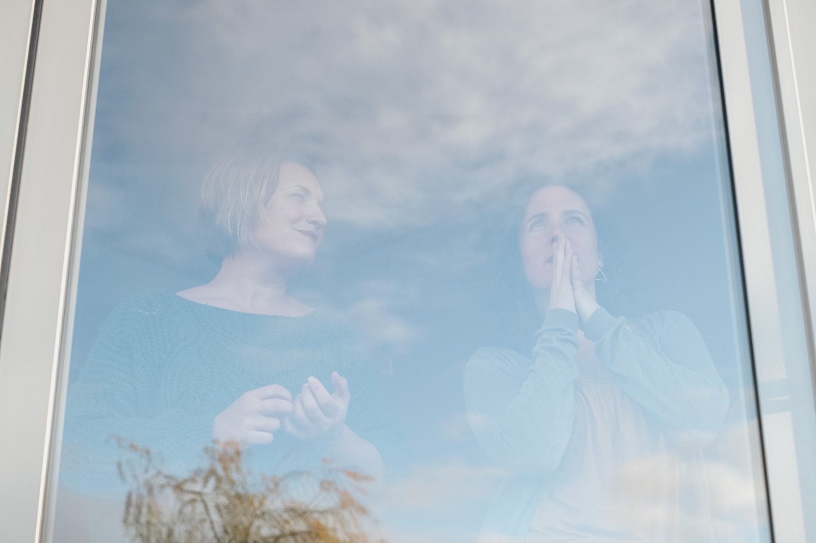 Twee vrouwen achter een raam, weerspiegeling van wolken en handen die iets uitleggen